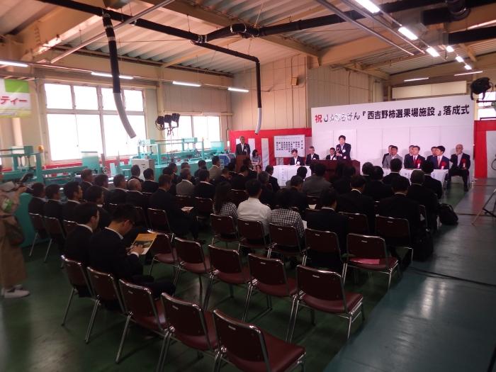 「祝JAならけん『西吉野柿選果場施設』落成式」の字を後ろに選果場を利用する生産者、JA、国会議員、行政機関関係者での落成式の写真