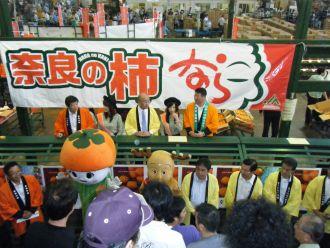 「奈良の柿」と書かれた看板に集まる人々の写真