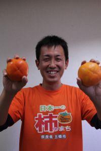 柿振興室職員が富有柿を両手に持っている、笑顔の写真