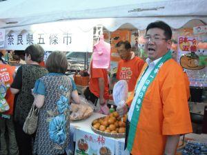 ハッピを着た五條市市長が八尾市で柿PRをしている写真