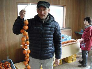 皮むきした柿を紐で吊り、その柿を持っている吉本農園の方の写真