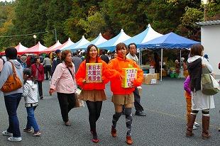 オレンジのジャンバーを着た女性が東日本大震災義援金の箱を持って歩いている写真