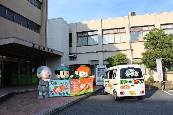五條市役所前で横断幕を広げるマスコットキャラクターゴーカスターたちと五條市PR用車両の写真