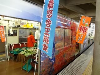電車の出入り口に農悠舎王隠堂と書かれたのぼりと電車の内部で野菜が販売されている写真