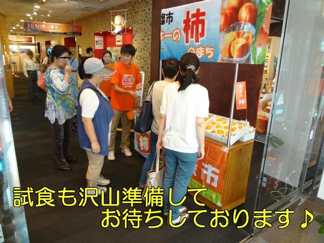 試食も沢山準備してお待ちしております。柿の試食をお客さんへ勧めるオレンジの柿Tシャツを着ている男性の写真