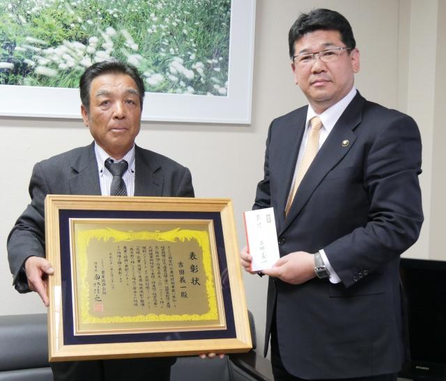 額縁に入った表彰状を持っている吉田さんと寄付金の袋を持っている市長の写真