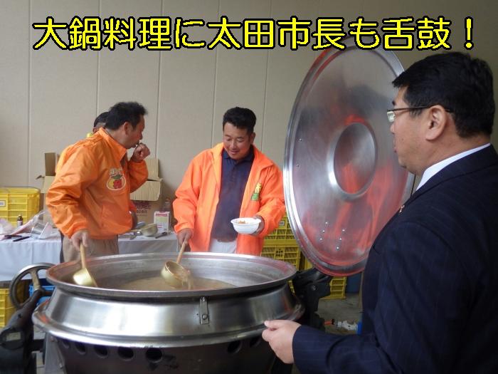 2人の男性が鍋より料理をお椀に注いでいるのを見ている市長の写真