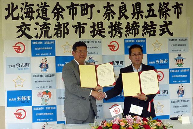 垂れ幕の前で、嶋余市町長と太田五條市長が握手を交わしている写真