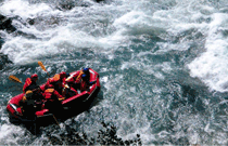 川の上で、5人がボートを漕いでラフティングをしている写真